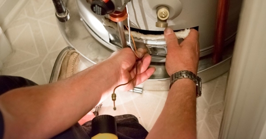 Man shines flashlight on hot water heater